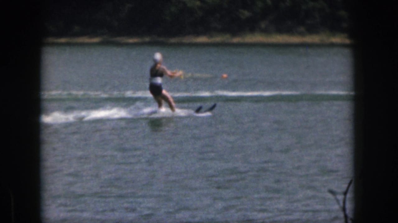 1961 Michigan home-movie frame of a woman water skier leaning slightly as she follows a tow rope across open lake water.