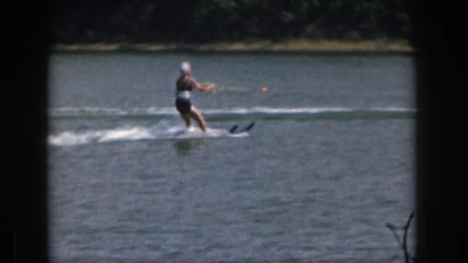 1961 Michigan home-movie frame of a woman water skier leaning slightly as she follows a tow rope across open lake water.