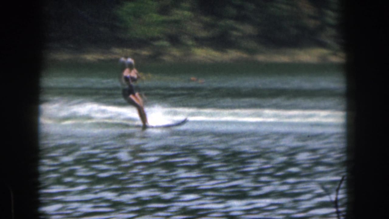 Water skier leans back while holding a tow rope on a rippled lake.