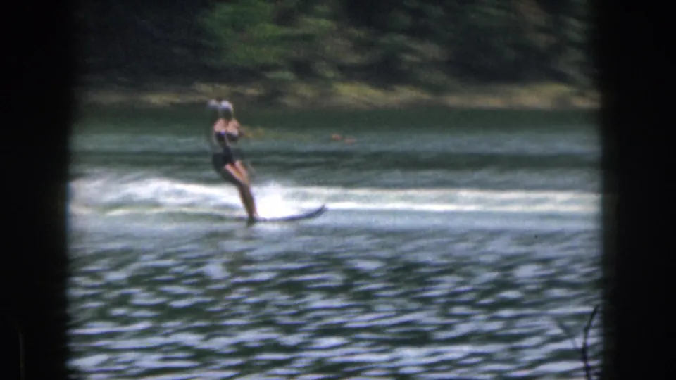 The woman water skier appears farther across the Michigan lake, leaning against the tow rope with spray trailing behind her skis.