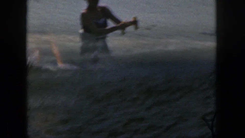 1961 Michigan lake footage showing the skier partly silhouetted while the tow rope crosses the water.