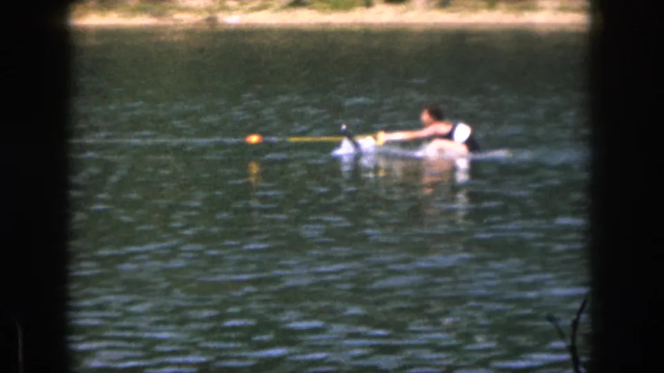1961 Michigan 8mm frame showing a person preparing to water ski, holding a yellow tow rope near an orange buoy on lake water.