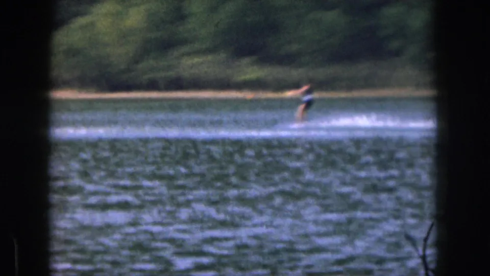 Distant skier in dark swimwear moves across a Michigan lake in soft 8mm footage from 1961.