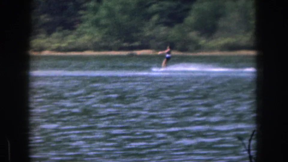 1961 Michigan lake scene with a distant water skier leaning into the tow line as spray trails behind.