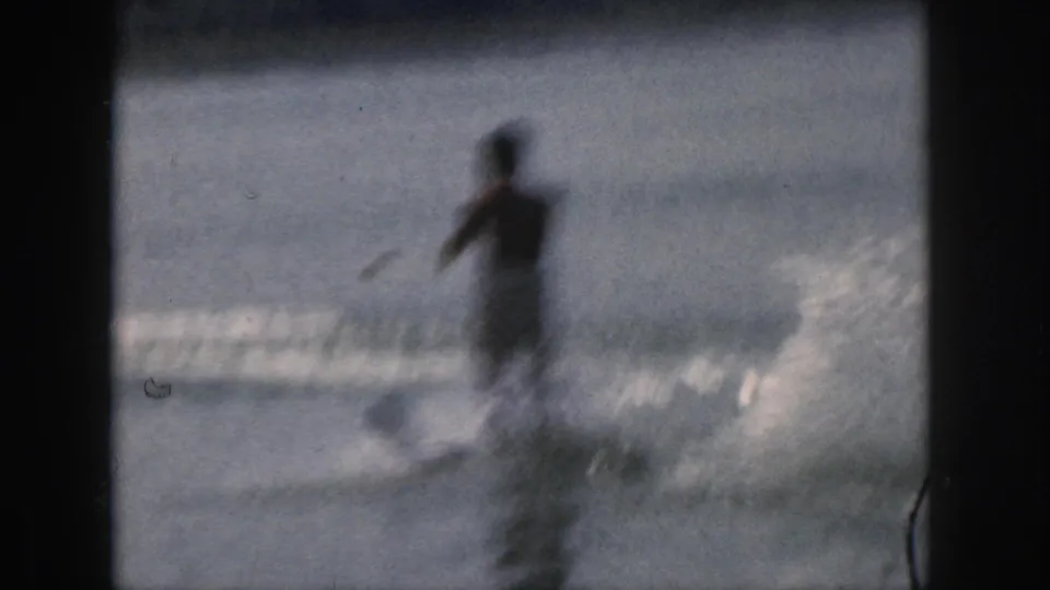 The adult skier appears soft and motion-blurred as he moves through lake spray in this 1961 Michigan 8mm home-movie frame.