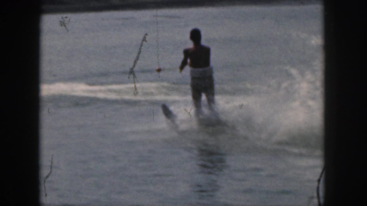 1961 Michigan 8mm frame showing a man water skiing on a calm lake, with tow rope, spray, and visible film gate edges.