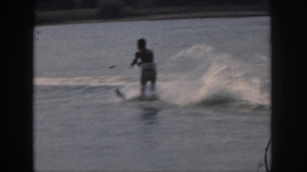 Water skier seen from behind crossing the lake as spray curls to one side.