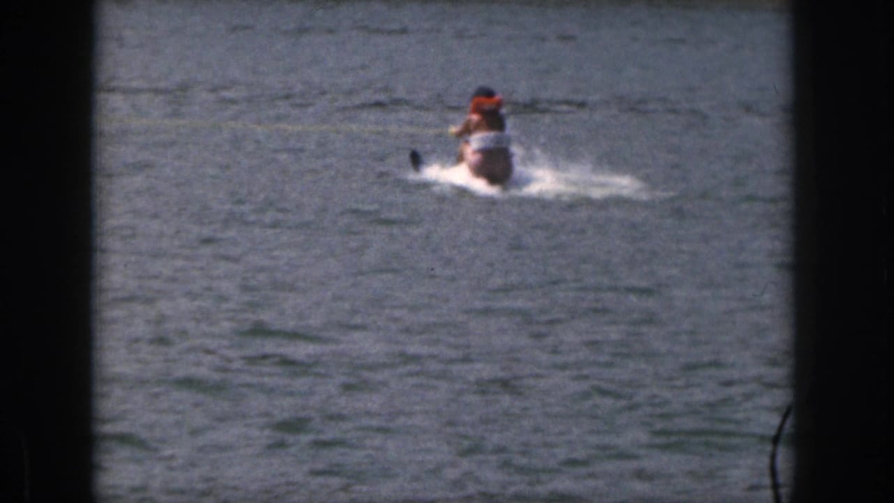 1961 Michigan home-movie frame with a small motorboat and a water skier moving across open lake water.
