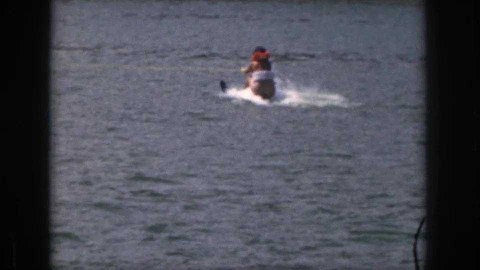 1961 Michigan home-movie frame with a small motorboat and a water skier moving across open lake water.