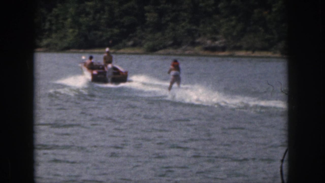 1961 Michigan 8mm frame showing a woman water skiing behind a small motorboat on a wooded lake.