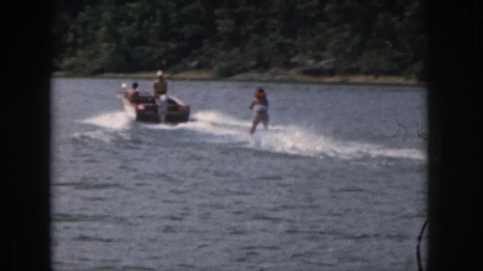 1961 Michigan 8mm frame showing a woman water skiing behind a small motorboat on a wooded lake.