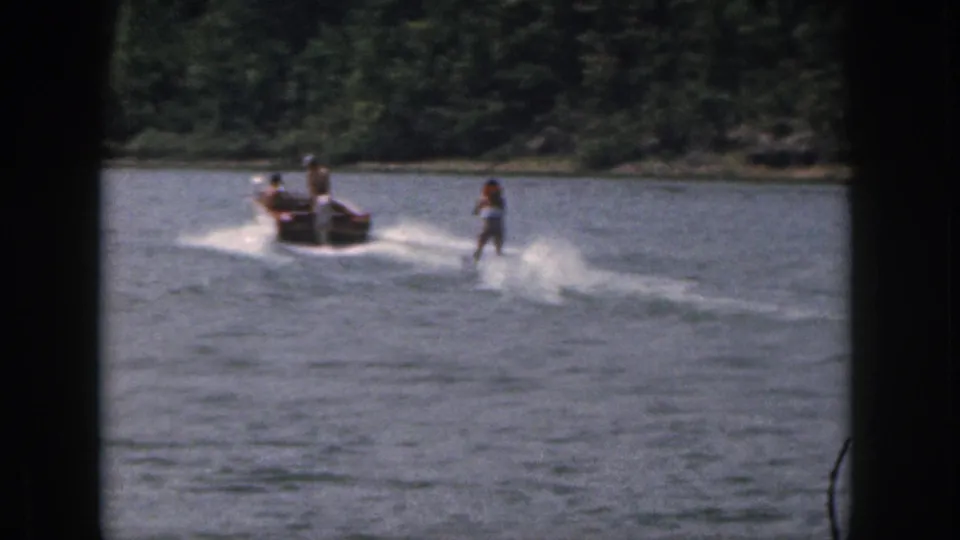 1961 Michigan home-movie frame of a distant woman water skier following a motorboat across a lake.