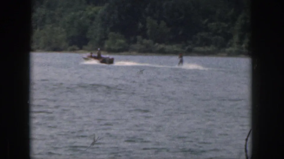 Final 1961 Michigan 8mm frame with a motorboat towing a distant skier across open water near a green shoreline.