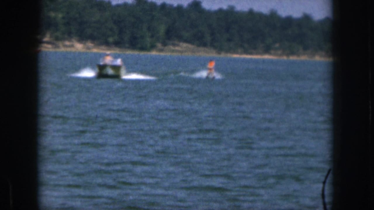 Distant boat and water skier moving across open water with a forested shoreline behind.