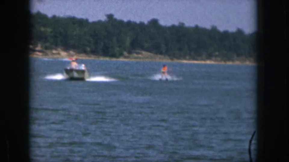 1961 Michigan 8mm frame showing a boat towing a water skier, seen from a distant home-movie viewpoint across the lake.