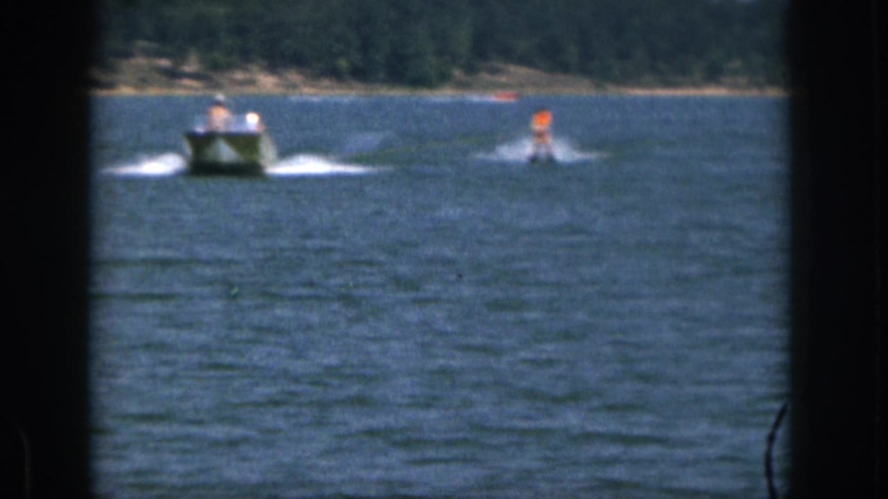 1961 Michigan 8mm frame showing a motorboat pulling a distant waterskier in an orange life vest across open lake water.