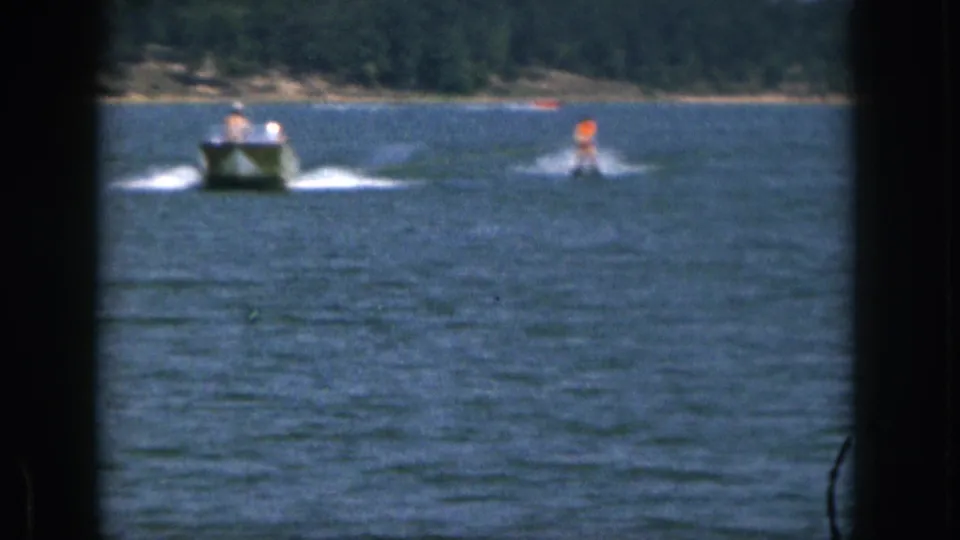 1961 Michigan 8mm frame showing a motorboat pulling a distant waterskier in an orange life vest across open lake water.