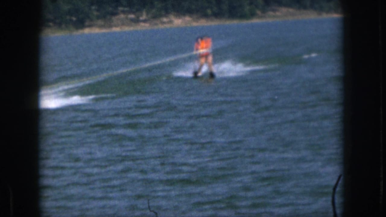 1961 Michigan home-movie frame with a waterskier in an orange life vest being pulled across a calm lake.