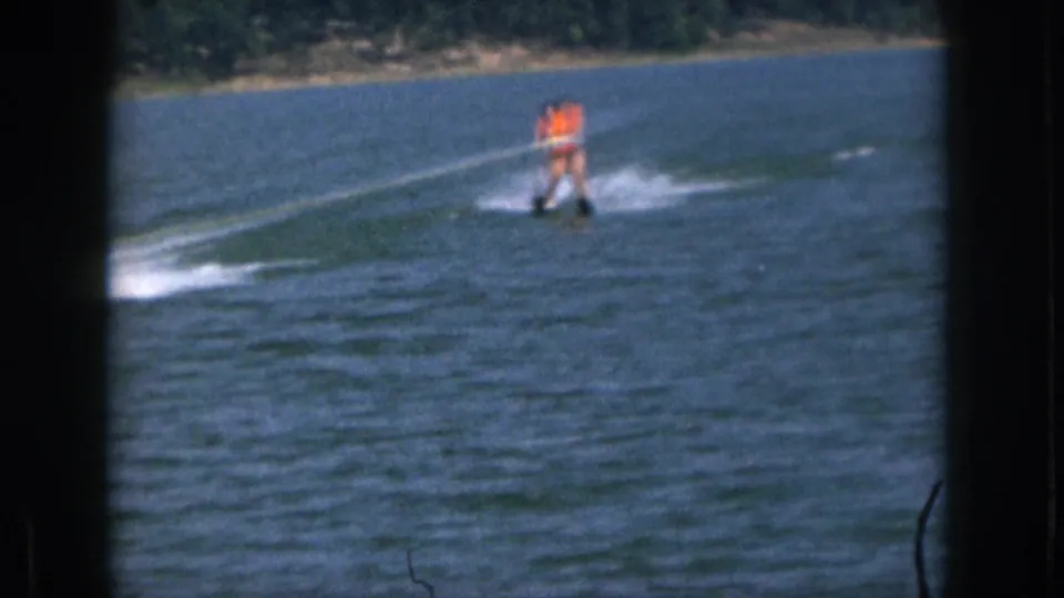 1961 Michigan home-movie frame with a waterskier in an orange life vest being pulled across a calm lake.