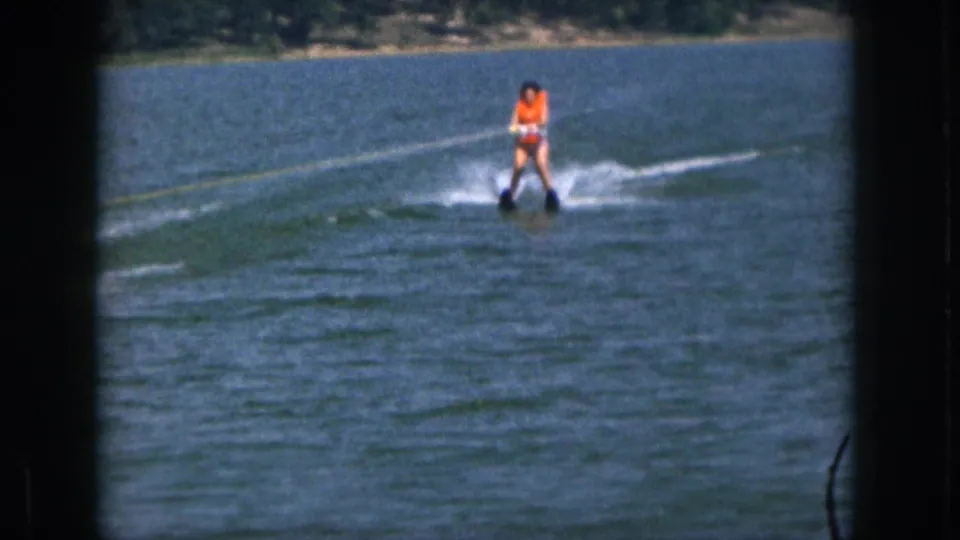 1961 Michigan 8mm frame showing a waterskier closer to camera, holding the tow rope while crossing the lake.