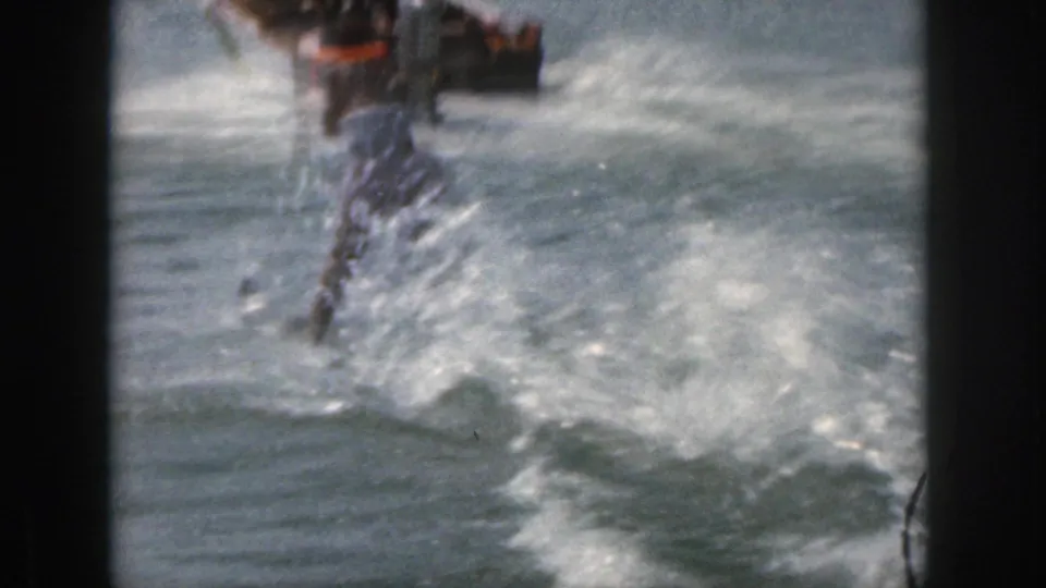 The water skier appears to lose balance and splash into the Michigan lake, with the tow rope and churned water visible in the frame.