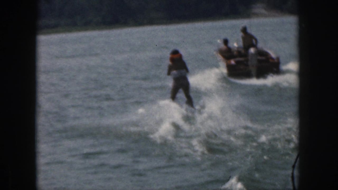 Water skier moves farther from the camera while a motorboat pulls ahead on the lake.