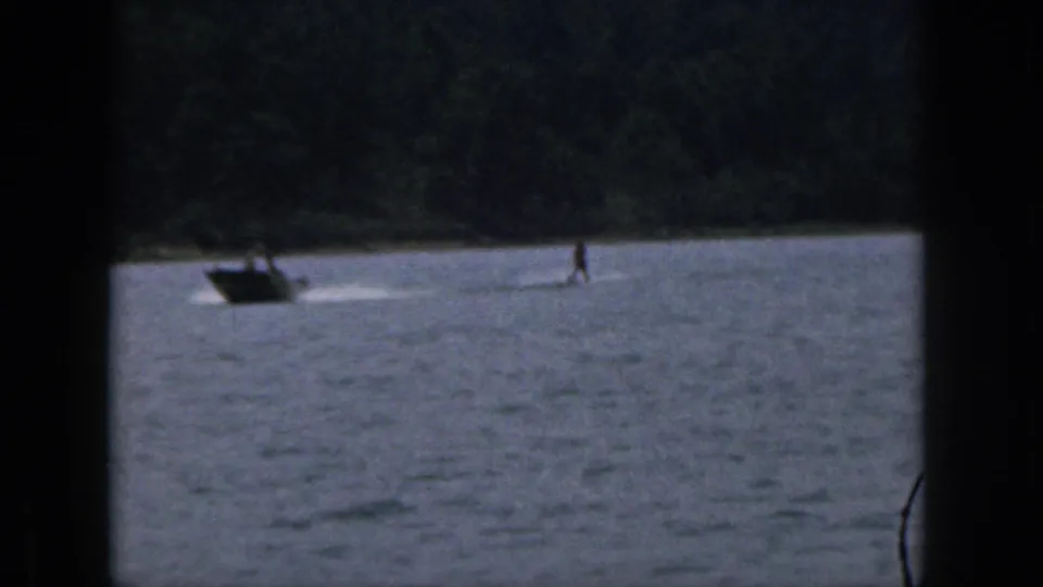 Wide 1961 Michigan home-movie view with a small boat at left and a distant water skier near the shoreline.