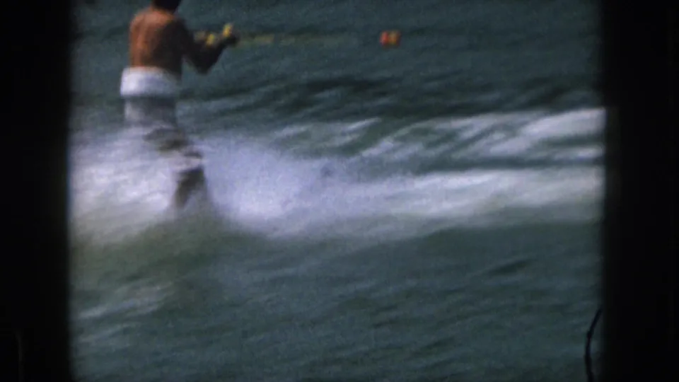 1961 Michigan 8mm frame with an adult water skier receding left as a long band of spray crosses the lake surface.