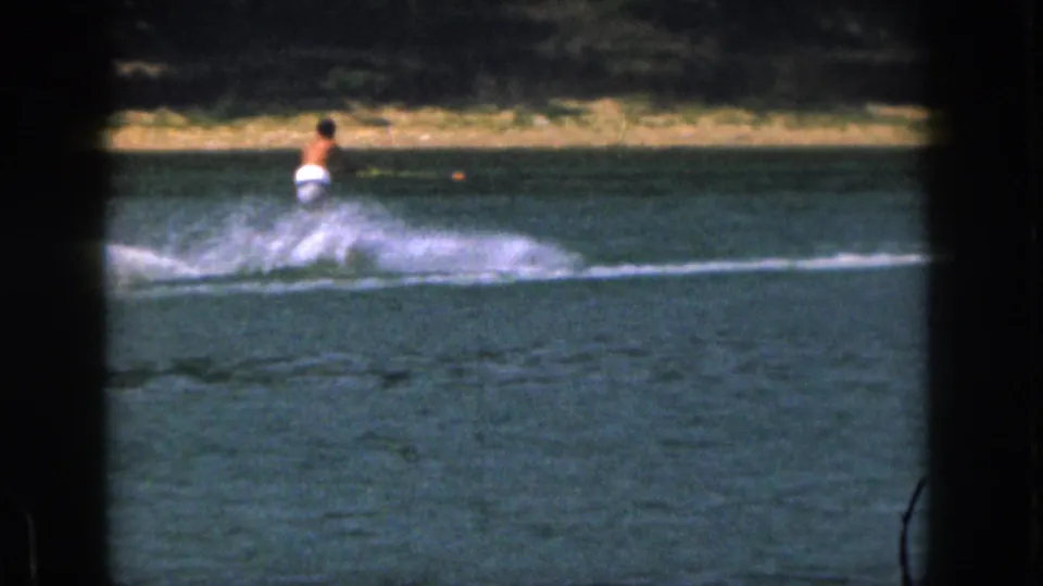 1961 Michigan 8mm frame of a water skier seen from behind at distance, with broad spray over the lake surface.