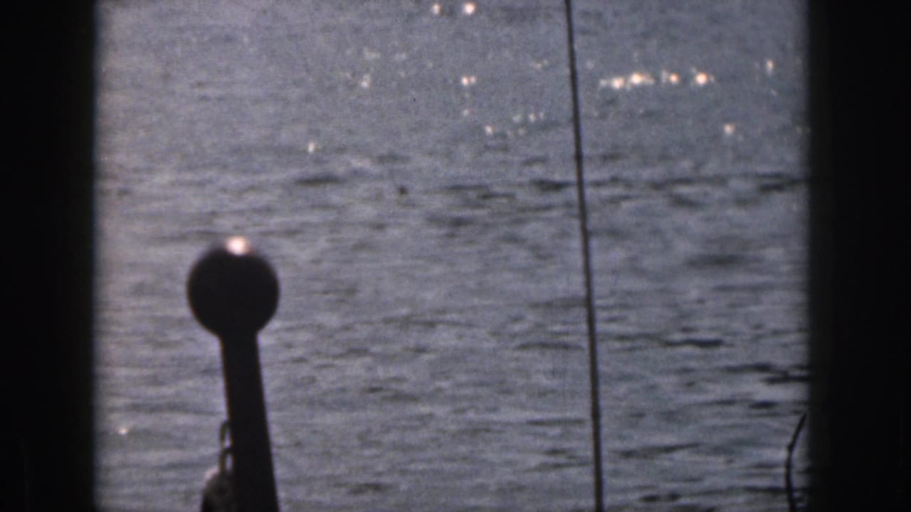 1961 Michigan 8mm frame showing open water through dark boat framing, with glare on the surface and a small structure at the edge.