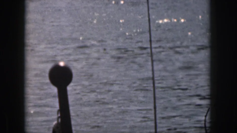 1961 Michigan 8mm frame showing open water through dark boat framing, with glare on the surface and a small structure at the edge.