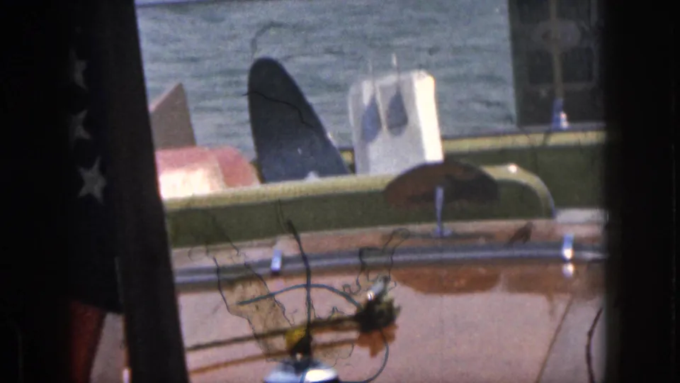 1961 Michigan 8mm frame showing a classic boat interior with green seating, varnished deck, steering wheel, and water in the background.