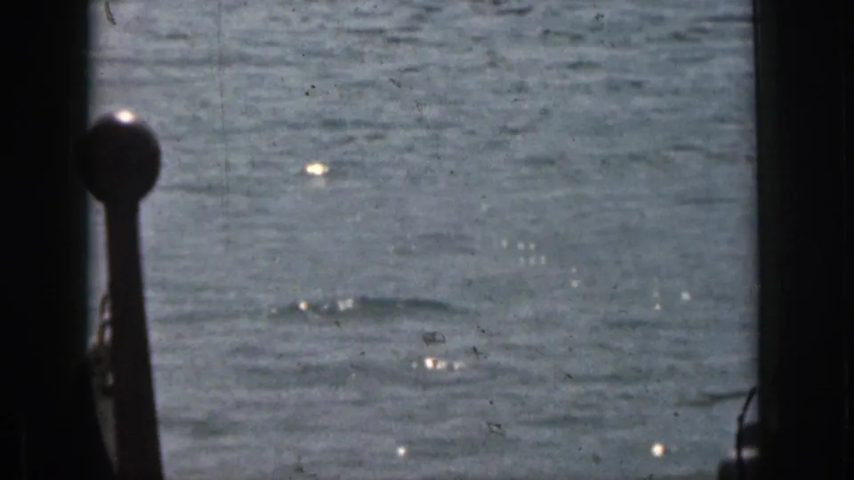 Rippled Michigan lake water in a 1961 8mm home-movie frame, seen through dark foreground framing with no clear person visible.