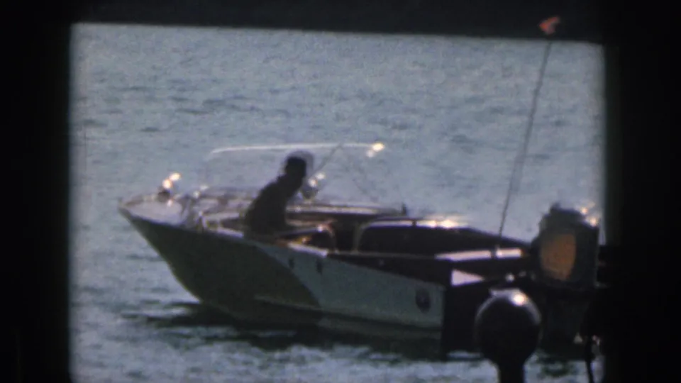 1961 Michigan home-movie frame with a close motorboat in the foreground and lake water beyond.