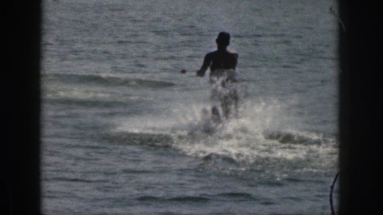 1961 Michigan 8mm frame showing a silhouetted person water skiing across a lake, with white spray and dark frame borders.