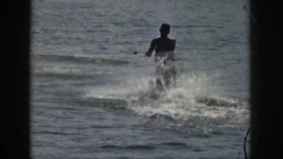 1961 Michigan 8mm frame showing a silhouetted person water skiing across a lake, with white spray and dark frame borders.