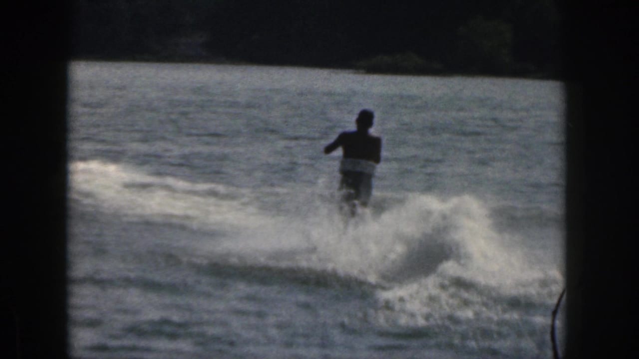 Water skier seen farther away, crossing the lake through a dark film border.