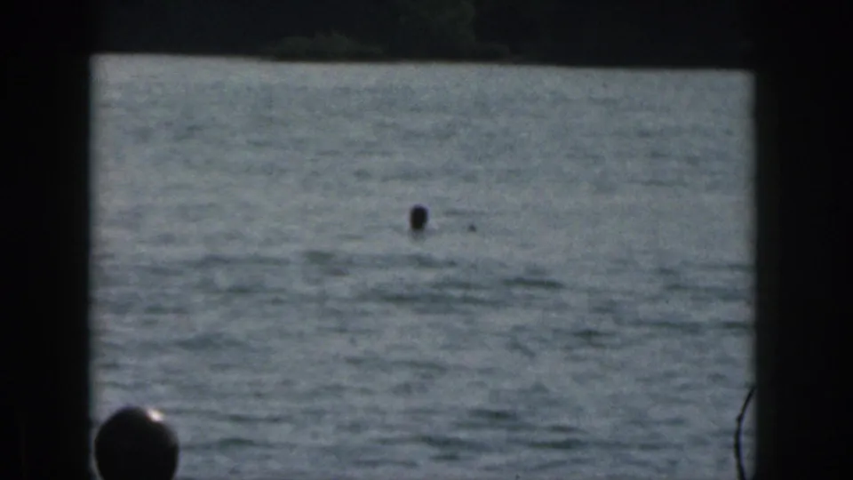 1961 Michigan home-movie frame with the skier mostly submerged, only a small head visible above the lake surface after the fall.