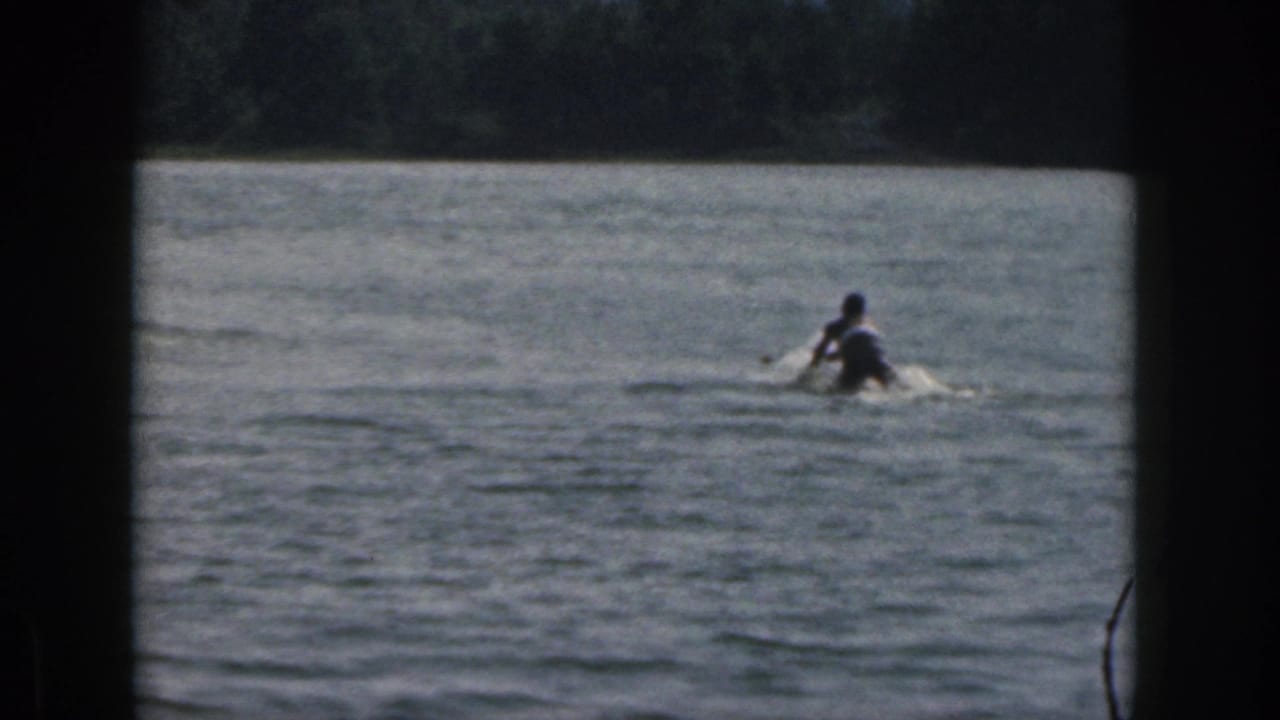 A water skier moves across a Michigan lake in 1961, seen at a distance with splash and 8mm frame edges.