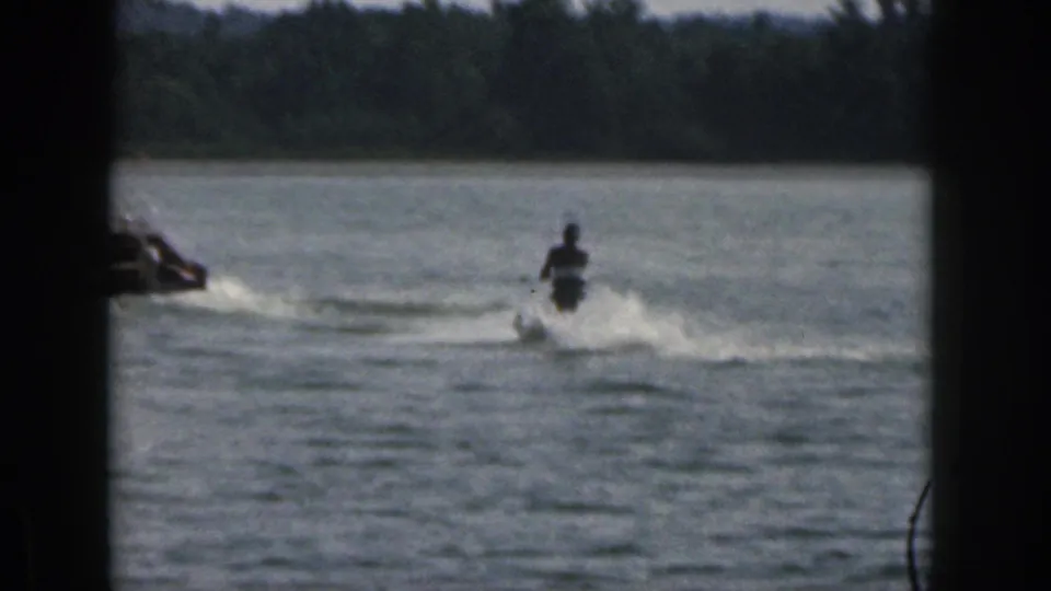 A water skier creates spray on a Michigan lake in 1961 as a tow boat enters the left edge of the frame.