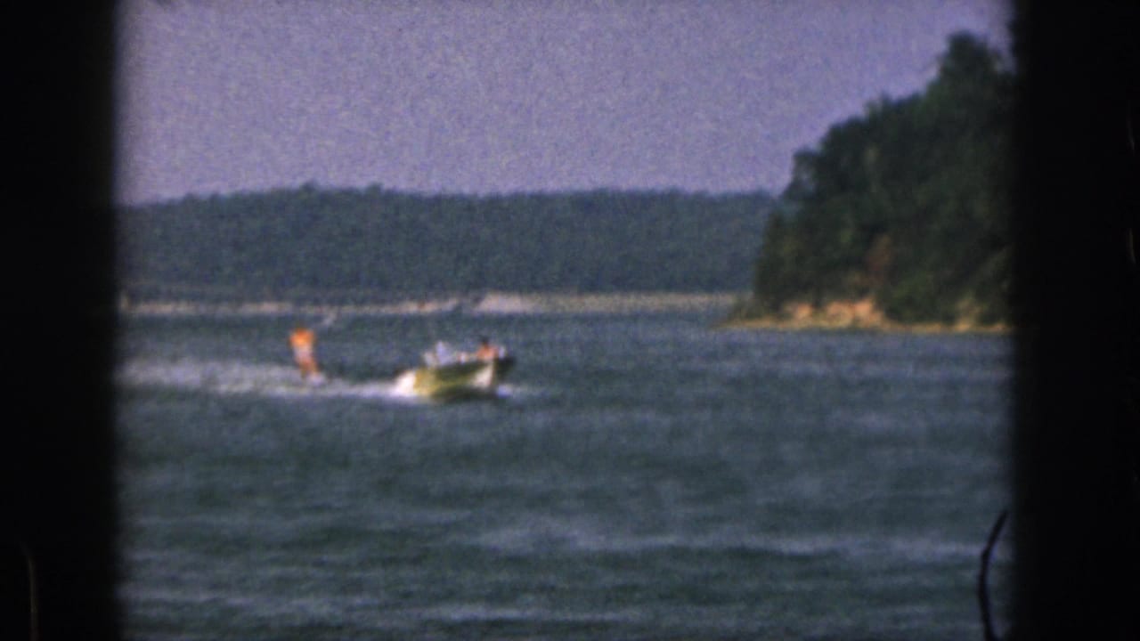 Small speedboat pulls a water skier across a lake near a wooded shoreline.