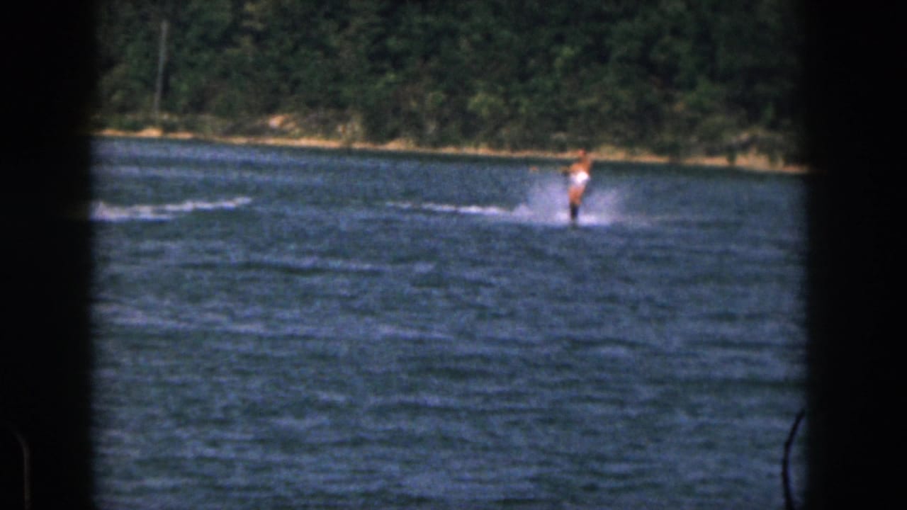 Water skier moving across open water with trees along the far bank.