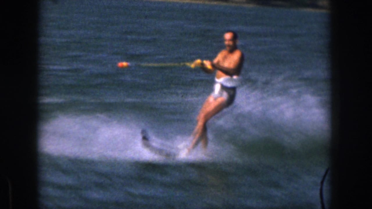Man in white swim trunks water skiing while holding a yellow tow rope on a lake.