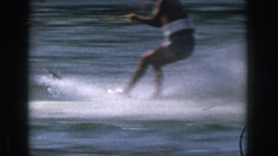 The final frame shows a cropped close view of the skier passing through heavy lake spray in 1961 Michigan home-movie footage.