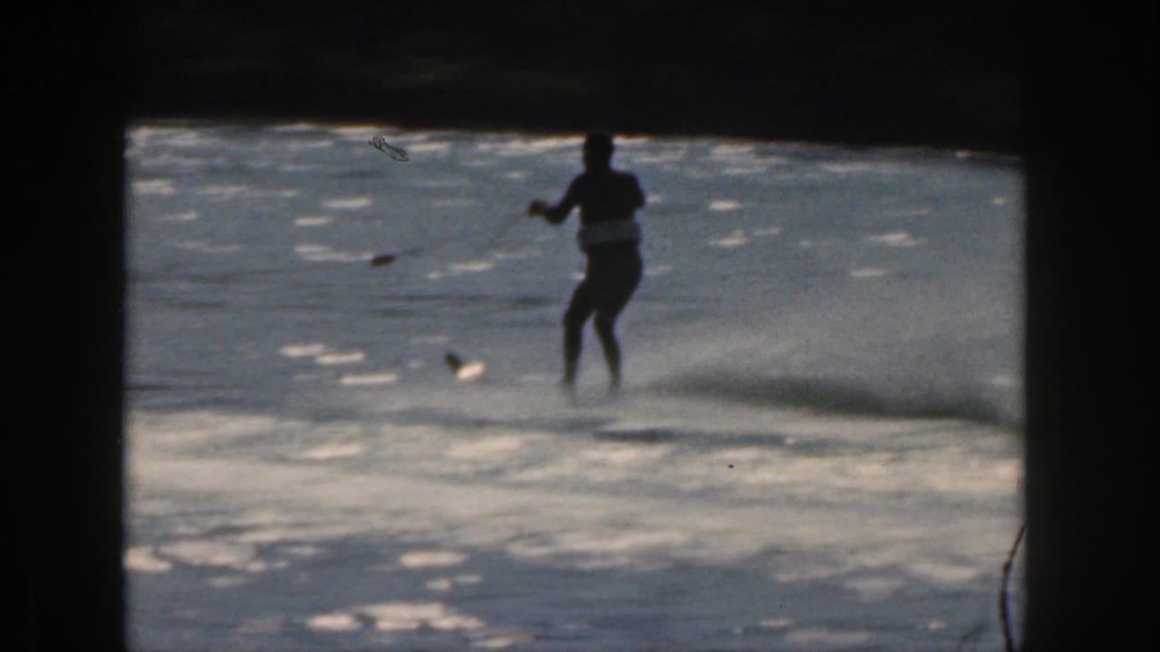 Distant water skier on a lake framed by dark projector borders and bright water reflections.