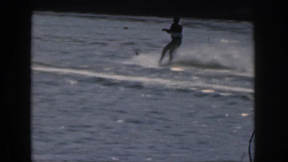 A man in dark swimwear leans while water skiing on a Michigan lake, captured in soft 1961 8mm home-movie footage.