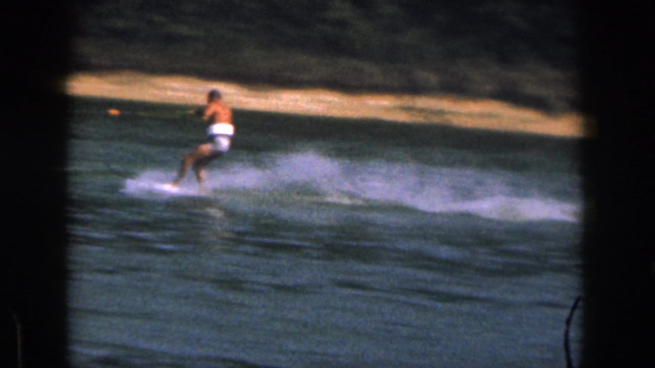 Water skier leans over the lake while holding a tow rope, with spray spreading behind him.