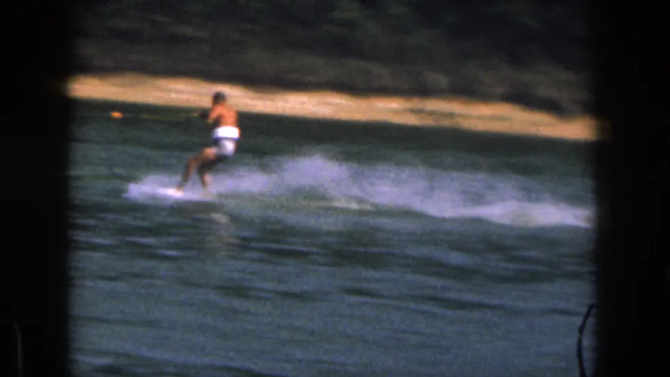 1961 Michigan home-movie frame of a man water skiing near shore, partly framed by dark 8mm projection borders.