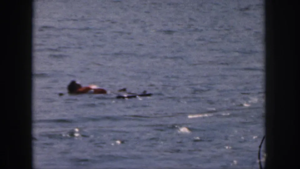 1961 Michigan home-movie frame showing the fallen skier floating in open lake water next to a ski or board.