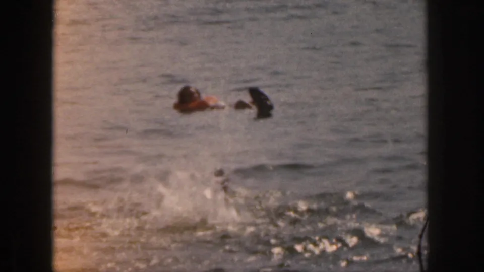 1961 Michigan home-movie frame with two people in life vests close together on open water and bright splashing in the lower foreground.